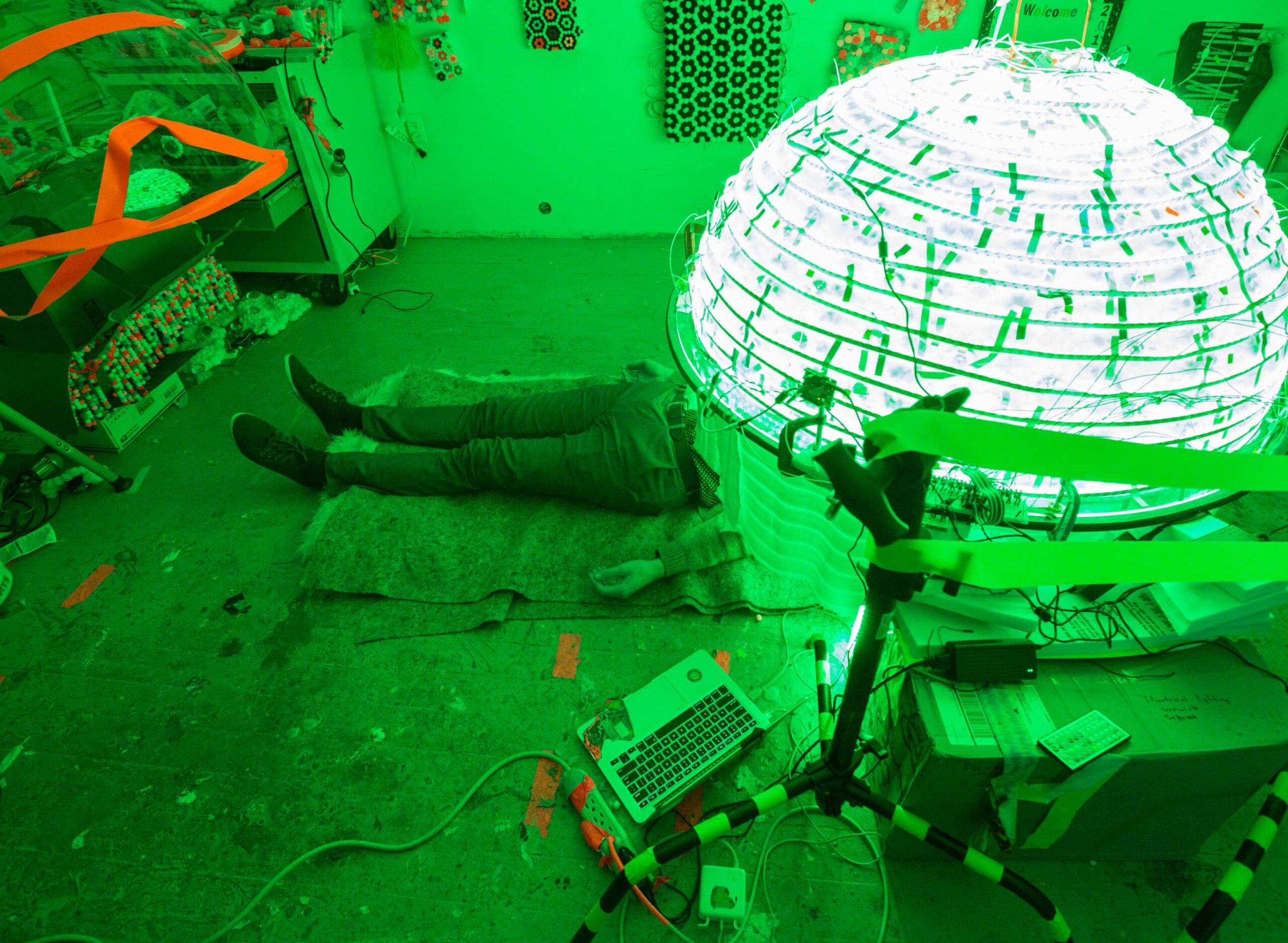 Room illuminated in green light, a person lying on the floor and a large illuminated ball.